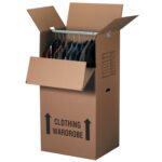 An open-top cardboard wardrobe box from the MH-USA 24 x 20 x 46 Wardrobe Boxes (5/Bundle) displays assorted clothes on a metal rod inside, labeled CLOTHING WARDROBE with two upward arrows.