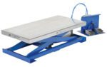 The Vestil Pneumatic Scissor Lift Table 200 Lb features a blue hydraulic scissor lift with a silver platform, foot pedal-controlled via a blue hose, and is showcased in its lowered position for lifting heavy objects efficiently.