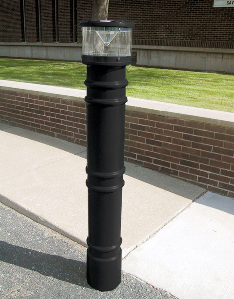 BPC-DM-LUV-B_A.jpg A paved pathway beside a brick wall features a black bollard with a transparent, dome-shaped light resembling the 57-inch Vestil Metro-Black Bollard Cover W/Light. Grass and a building can be seen in the background.
