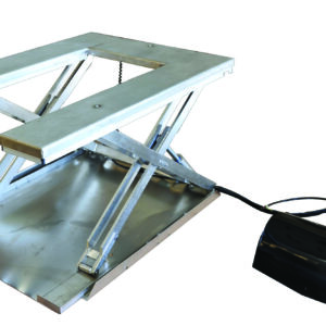 The Vestil Low Profile Stainless Steel Elec U Lift Table has a metallic scissor lift platform with a rectangular surface, powered by a hydraulic mechanism. A cable links it to a black control box featuring yellow and red emergency stop buttons, highlighting its slightly raised position.