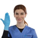 A person with red hair is wearing a blue medical scrub top and a blue glove on their right hand, which is raised in a wave. They are smiling and standing against a white background.