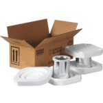An open MH-USA 10 1/4 x 5 1/8 x 6 3/16 box displays its label, surrounded by white foam packaging from the Foam Haz Mat Shipper Kit. The foam securely holds a cylindrical silver-finished metal part.