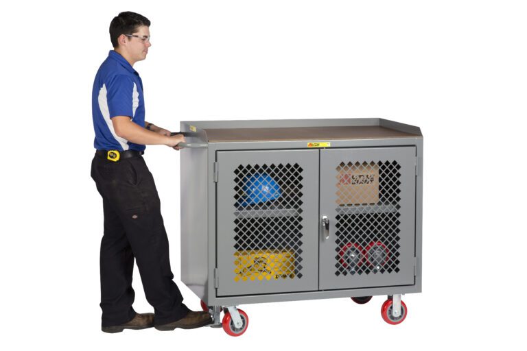 A person in a blue shirt and black pants, with a tape measure at their belt, pushes a Little Giant Mobile Bench Cabinet with Clearview Doors. The gray cabinet, loaded with tools and equipment, moves smoothly on red casters as they navigate the space.