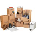 The MH-USA Deluxe Home Moving Kit is being used with stacked boxes labeled Fragile and Clothing Wardrobe, containing items like toys, two coffee makers, clothes on hangers, and packing materials. It includes a wine glass divider to protect your glassware during transit.