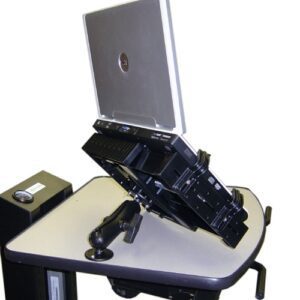 A laptop is mounted on a mechanical arm positioned at an angle on a desk. The setup is designed for ergonomic adjustment. A small speaker or electronic device is visible on the desk to the left.