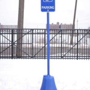 Against a snowy backdrop with a fence, the tall parking sign featuring a wheelchair symbol for accessible parking stands securely on the Vestil Octagon Sign Base Blue 8 X 8 X 98.