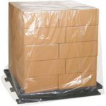 A stack of cardboard boxes neatly aligned in rows and columns sits on a black pallet, protected by MH-USA 48 x 46 x 96 - 2 Mil Clear Pallet Covers (50/Case).