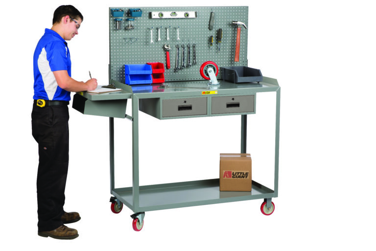 A person in a blue and white shirt writes on a clipboard at a gray Little Giant Work Height Mobile Workstation, with tools, a hammer, two blue bins on the bench, and a cardboard box on the lower shelf above two drawers.