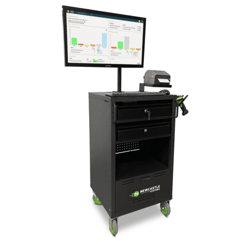 A mobile workstation with a monitor displaying graphs and data analysis. The black cart features a keyboard shelf and storage drawers. It has green wheels and branding for Newcastle Systems. A printer or scanner is on top of the cart.