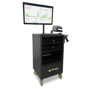 A mobile workstation with a monitor displaying charts and data, a printer, and a handle. It has a black cabinet with drawers and green wheels, labeled Newcastle Systems.