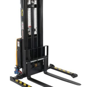 The Vestil Adj Stacker W/Pwr Lift 137In Power Traction Drive is a black industrial pallet stacker with dual long forks, a vertical lifting mechanism, control levers, warning labels, and yellow-black safety stripes on the forks.
