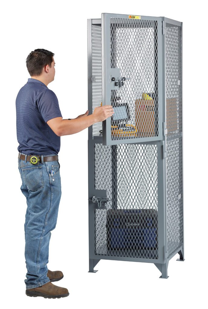 A person in a blue shirt and jeans opens a tall, gray Little Giant Two Compartment Compact Storage Locker containing a cardboard box and assorted items. A tape measure hangs from their belt as they inspect the contents.