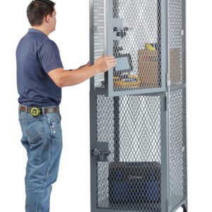 A person in a blue shirt and jeans opens a tall, gray Little Giant Two Compartment Compact Storage Locker containing a cardboard box and assorted items. A tape measure hangs from their belt as they inspect the contents.
