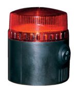 A compact, cylindrical black alarm with a ribbed red lens at the top, similar to the Vestil Light & Siren for Spring Loaded Bollard, featuring a power switch on its side. The translucent red lens is designed to glow when activated.