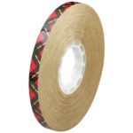 The 1/4 x 36 yds. 3M™ 924 Adhesive Transfer Tape, featuring a brown tone with a black and red plaid edge, elegantly wraps around its white plastic core. This tape adds subtle style to projects against a pristine white backdrop.