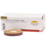 A roll of 1/4 x 36 yds. (6 Pack) 3M™ 969 Adhesive Transfer Tape, with a plaid side design, stands before its white and yellow box labeled High-Tack.