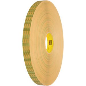 A large roll of 3M™ 465XL Adhesive Transfer Tape features a yellow core and brown outer layer with green text and patterns. It stands vertically against a white background. This 1/2 x 60 yds. roll is part of the 1/2 x 60 yds. (6 Pack) set, packaged as six per case.