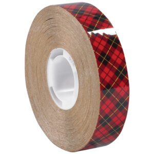 The 1/2 x 36 yds. 3M™ 976 Adhesive Transfer Tape, partially unspooled and wrapped around a white cylindrical core, features a red and black plaid pattern with thin yellow lines.