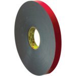 The 1 x 5 yds. Gray 3M™ 4646 VHB™ Tape, featuring a red backing and a yellow core, stands upright in its circular form. Its thickness indicates heavy-duty adhesiveness, perfect for various projects.