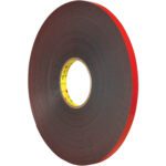 A 1/2 x 5 yds. roll of dark gray 3M™ 5925 VHB™ tape, with a red liner and black double-sided adhesive, stands vertically against a white background. Its yellow core with text adds color to this versatile essential.