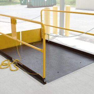 The Vestil Prem Truck Scissor Dock Lift 5K 6X8 Ft is equipped with bright yellow safety rails and a chain, anchored in concrete and accompanied by a yellow coiled cable. Nearby, bollards protect a building.