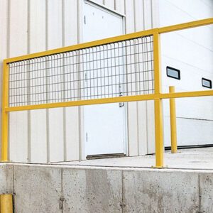 A sturdy yellow Vestil Steel Sq Safe Handrail Wire Mesh 108 In is installed on a concrete platform outside the beige-sided building. Beyond it, there’s a closed white door and a large overhead garage door with two small windows.