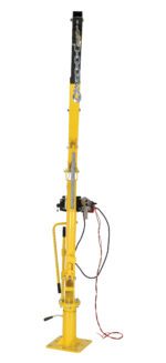 The yellow Vestil Winch Operated Truck Jib Crane - DC features a vertical arm, hydraulic lever, chain, and attached wires. Its designed for lifting heavy objects and has a sturdy base for stability.