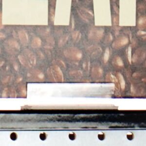 A close-up of a coffee machine framed by coffee beans and the partial word START, enhanced by an industrial charm from a silver metal surface and black vertical slots, reminiscent of Vulcan SP SIGN HOLDERs sleek design.