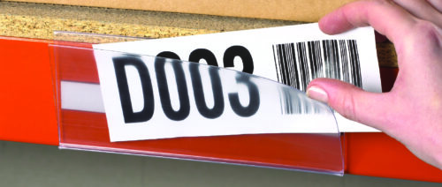 A person inserts a paper label with the code D003 and a barcode into a transparent holder on an orange shelf edge, enhancing warehouse designs by streamlining inventory management.