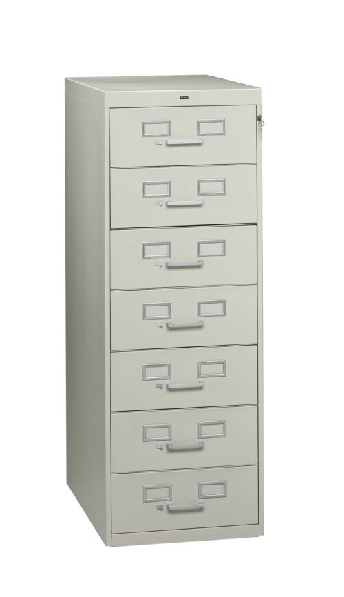 A tall, light gray filing cabinet with six drawers, each featuring a label holder and handle. The cabinet is slightly angled to the left, showing depth and structure.