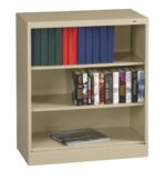 A beige metal bookshelf with three shelves. The top shelf holds blue and red binders. The middle shelf contains several Stephen King books. The bottom shelf has a single large book lying flat.