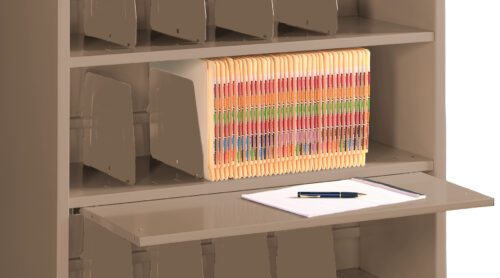 A beige filing cabinet with an open shelf showing a row of color-coded file folders. A pull-out shelf holds a clipboard with white paper and a black pen. Dividers are visible on the shelves, organizing the files.