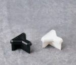 A black and a white plastic corner protector, shaped like a right angle, are placed on a light gray textured surface. They are designed to protect furniture or walls from damage.