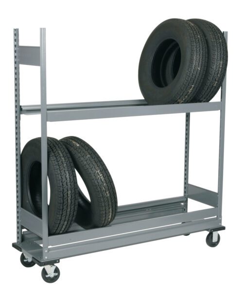 A gray metal shelving unit on wheels holding four car tires. Three tires are on the bottom shelf, one propped up against two lying flat, and one tire is on the top shelf, placed upright. The unit is in an empty space.