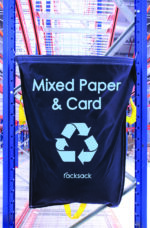 A blue MH-USA Racksack - Mixed Paper & Card hangs on metal shelving in a warehouse, featuring a white recycling symbol and the Racksack brand name at the bottom.