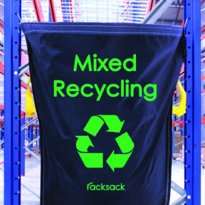 A blue MH-USA Racksack labeled Mixed Recycling, featuring a green recycling symbol and yellow side handles, hangs on a metal rack in an industrial setting.