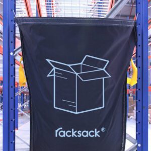 A large black MH-USA Racksack Symbol Only - Cardboard with a blue outline and bold racksack print is attached to blue metal shelves in a warehouse, hanging amidst orange and blue shelving units. In the background, cardboard boxes are neatly stacked.