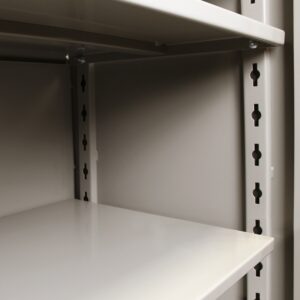 Close-up of a gray metal shelving unit with adjustable shelves. The vertical support features a series of holes for shelf height adjustment. The surface is smooth and unoccupied, emphasizing the shelfs versatility and industrial design.