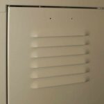 Close-up of a beige metal locker door with five horizontal vents in the center. The surface appears smooth with slight shadows emphasizing the vent openings.