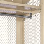 Close-up view of a beige metallic cage-like structure with diamond-patterned mesh walls. Inside is a horizontal metal rod, partially obscured, supported by metal brackets and hooks.