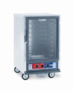 The Metro C515-PXFC-4A C5 1 Series Proofing Cabinet, a 1/2 Height stainless steel commercial food warmer with a clear glass front and wheels, runs on 1210-1440W. It includes fixed wire slides for trays and has bottom-front control knobs with red and blue indicators.