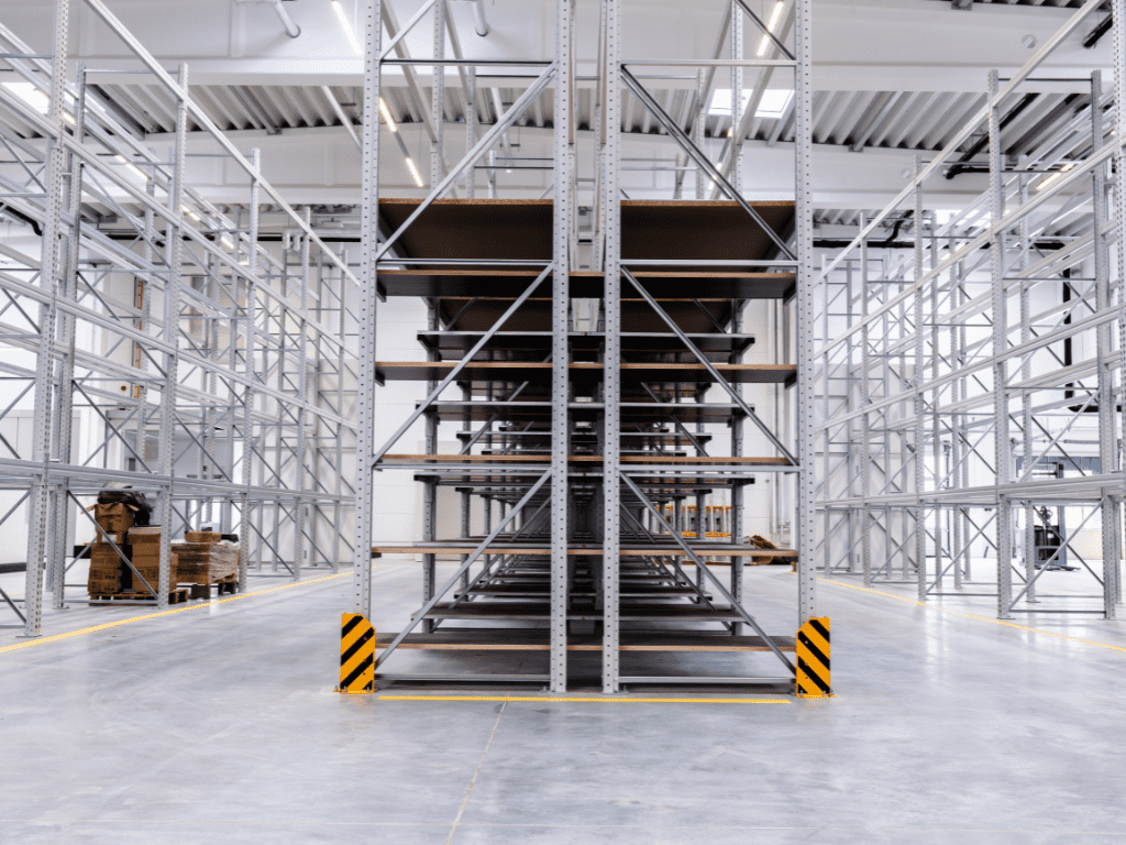 Empty industrial warehouse with tall, metal shelving units and a polished concrete floor, ready to transform your storage space. The shelves are unstocked, and the brightly lit area exudes openness, perfect for optimizing any storage needs.