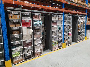 Warehouse shelves filled with various neatly organized bins and boxes, showcasing effective storage solutions for supplies and products. The aisle floor is clean, marked with yellow guide lines, ensuring efficient material handling.