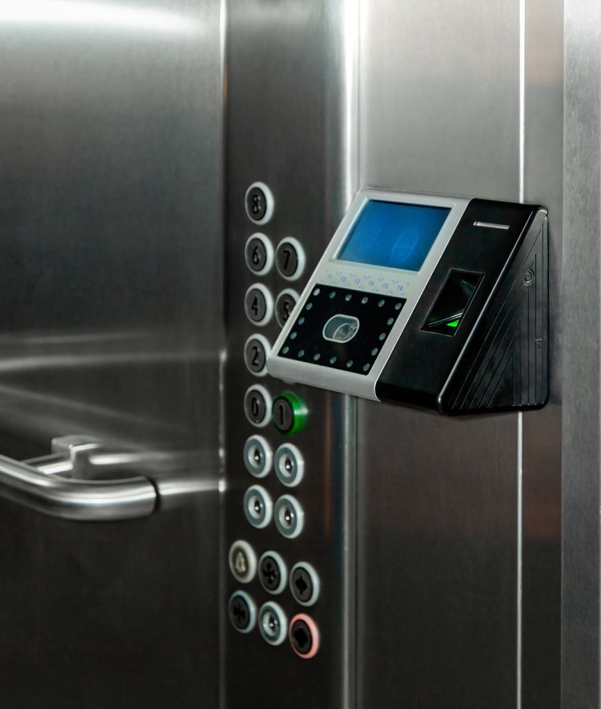 An elevator panel with a keypad of numbered buttons, featuring a modern digital display and biometric fingerprint scanner for secure access. The metallic interior includes a handrail, seamlessly incorporating convenient storage options like tenant storage lockers for added practicality.