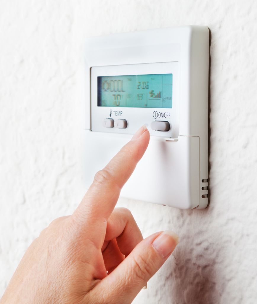 A hand adjusts a digital thermostat on a white wall, showcasing convenient storage options for your home environment. The display reveals temperature settings and other essential information as the hand presses the ON/OFF button.