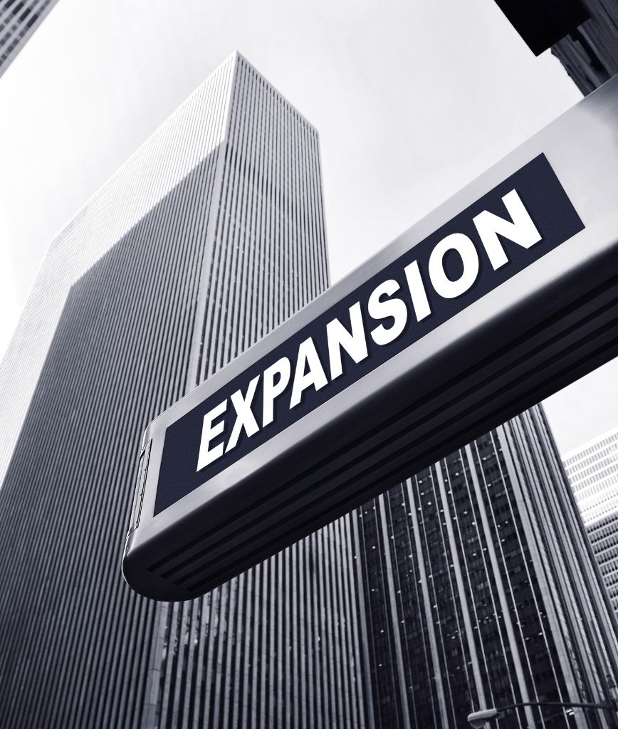 A street sign boldly displays EXPANSION in white against a black backdrop. Skyscrapers tower in the distance, defining a cityscape with a grayish, monochromatic tone—an ideal metaphor for property management amenities like tenant storage lockers nestled within urban growth.