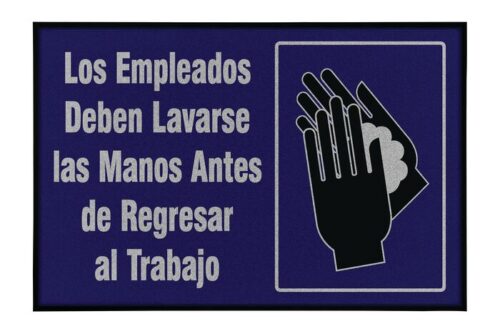A Justrite Mat, 194 Span Employee Wash 4X6, is placed beneath a sign in Spanish that says Los Empleados Deben Lavarse las Manos Antes de Regresar al Trabajo with a handwashing illustration against a dark blue background.