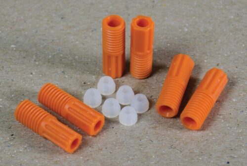 The Justrite 2.5 mm Tubing Connector Set features orange plastic dowels with ridges and small, white cone-shaped hollow caps, arranged on a textured beige surface.