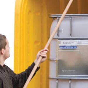 Using the Justrite IBC Outdoor Shed Reach Pole, a person opens a yellow containers lid, revealing a large white plastic storage tank with a front metal plate. The plain white background highlights the scenes simplicity.
