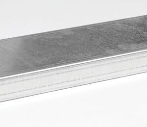 A rectangular metal drain grate with a textured surface and two slots on one side features a rugged design similar to that of a Justrite Shelf, 2G Mini Cabinet. It rests on a light gray background, angled to give depth and dimension.